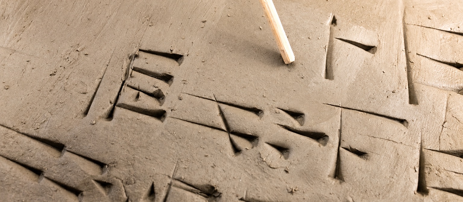 Uno stilo di legno accanto ai segni cuneiformi incisi nell’argilla